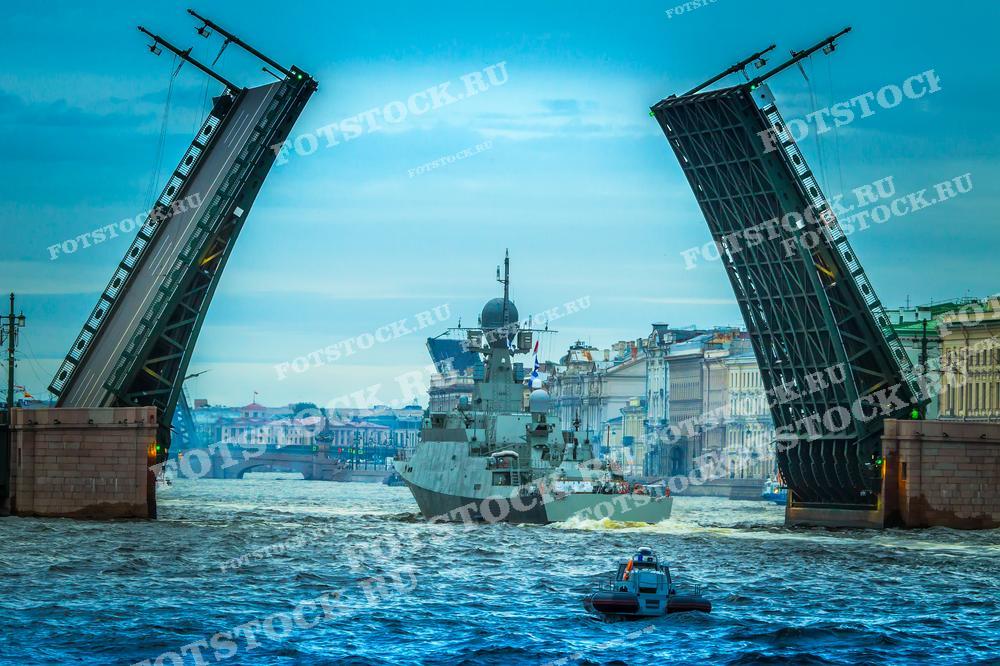 На фотографии запечатлён впечатляющий момент: военный корабль проходит под разведённым мостом на Неве в Санкт-Петербурге. Динамика сцены подчёркнута видом массивного корабля на фоне величественной исторической архитектуры города, создавая образ, наполненный силой и исторической значимостью. Это изображение отлично подойдёт для публикаций, посвящённых военно-морской тематике, истории Санкт-Петербурга, а также для туристических гидов, демонстрирующих уникальные моменты жизни города.
